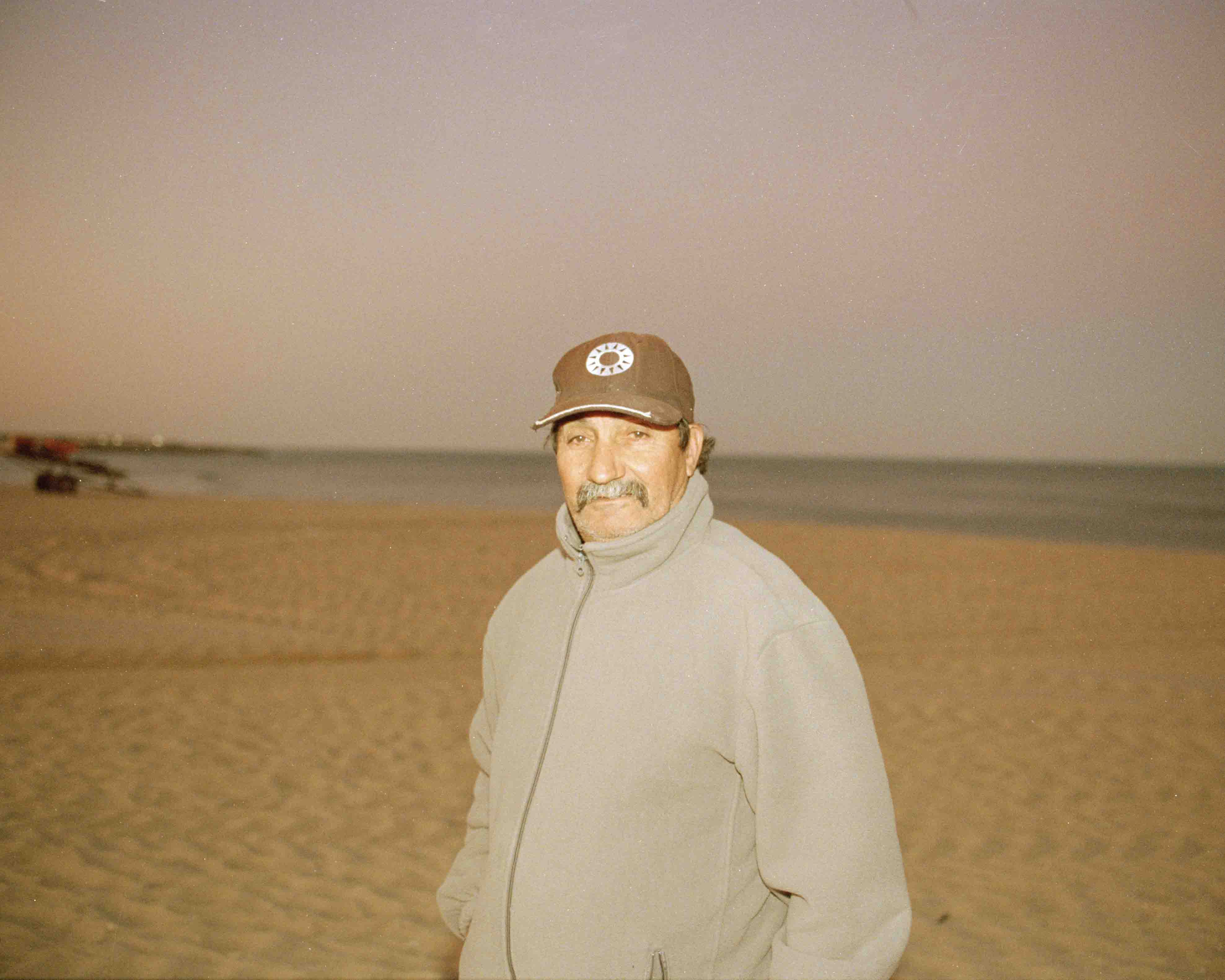 Portrait of a Fisherman, his name is Américo. He is standing on the beach he works at with the sea behind him. The photo was taking at sunrise after Américo came from the sea.