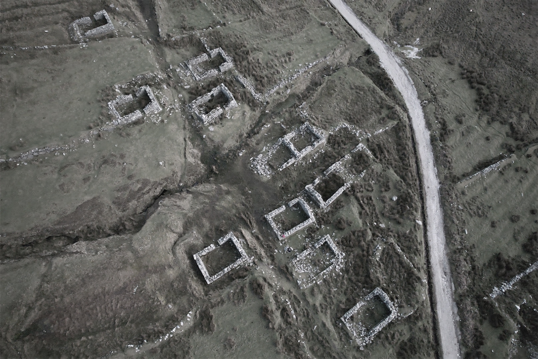 a drone image of approximately 10 stone cottages with a stone road running alongside