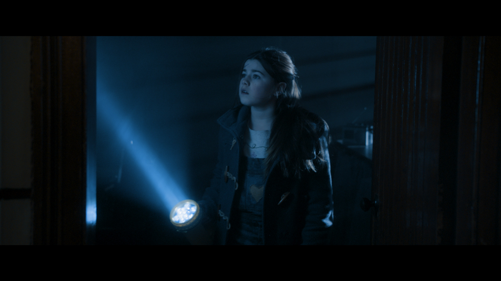 A young girl holds a torch in a dark room.