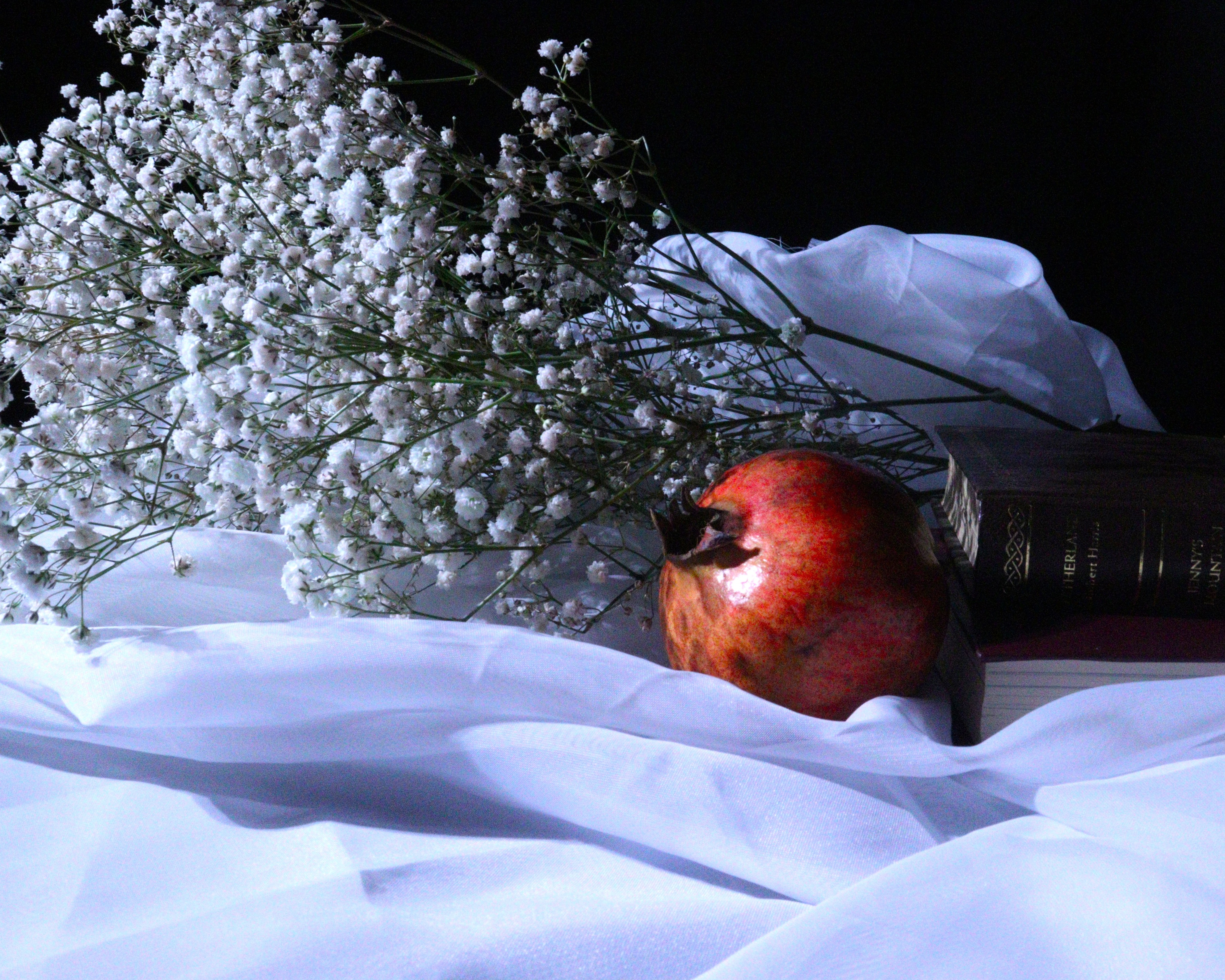 A pomegranate, babies breath and book laying on a veil