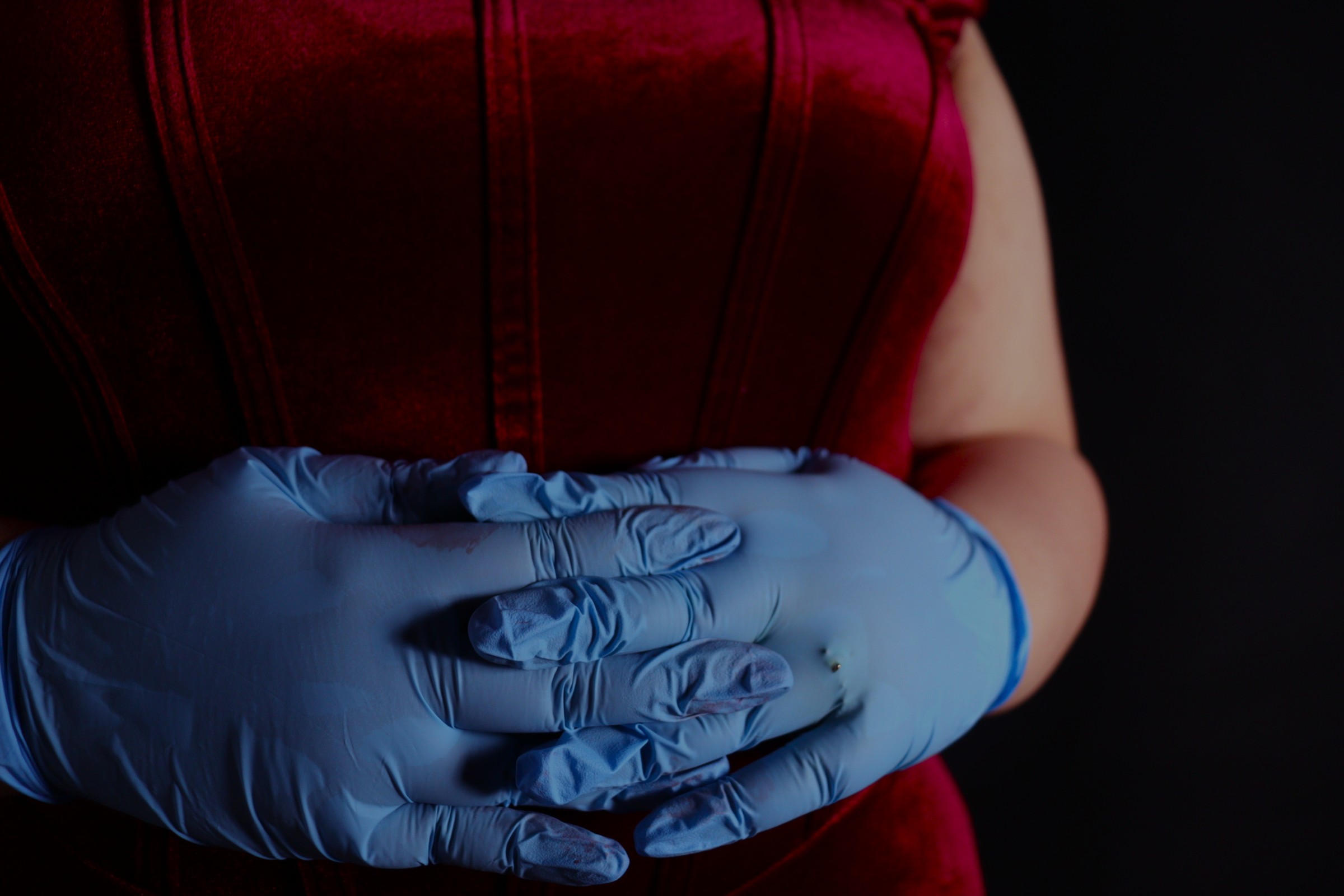Woman in red with latex gloves, her hands are tightly clasped in front of her
