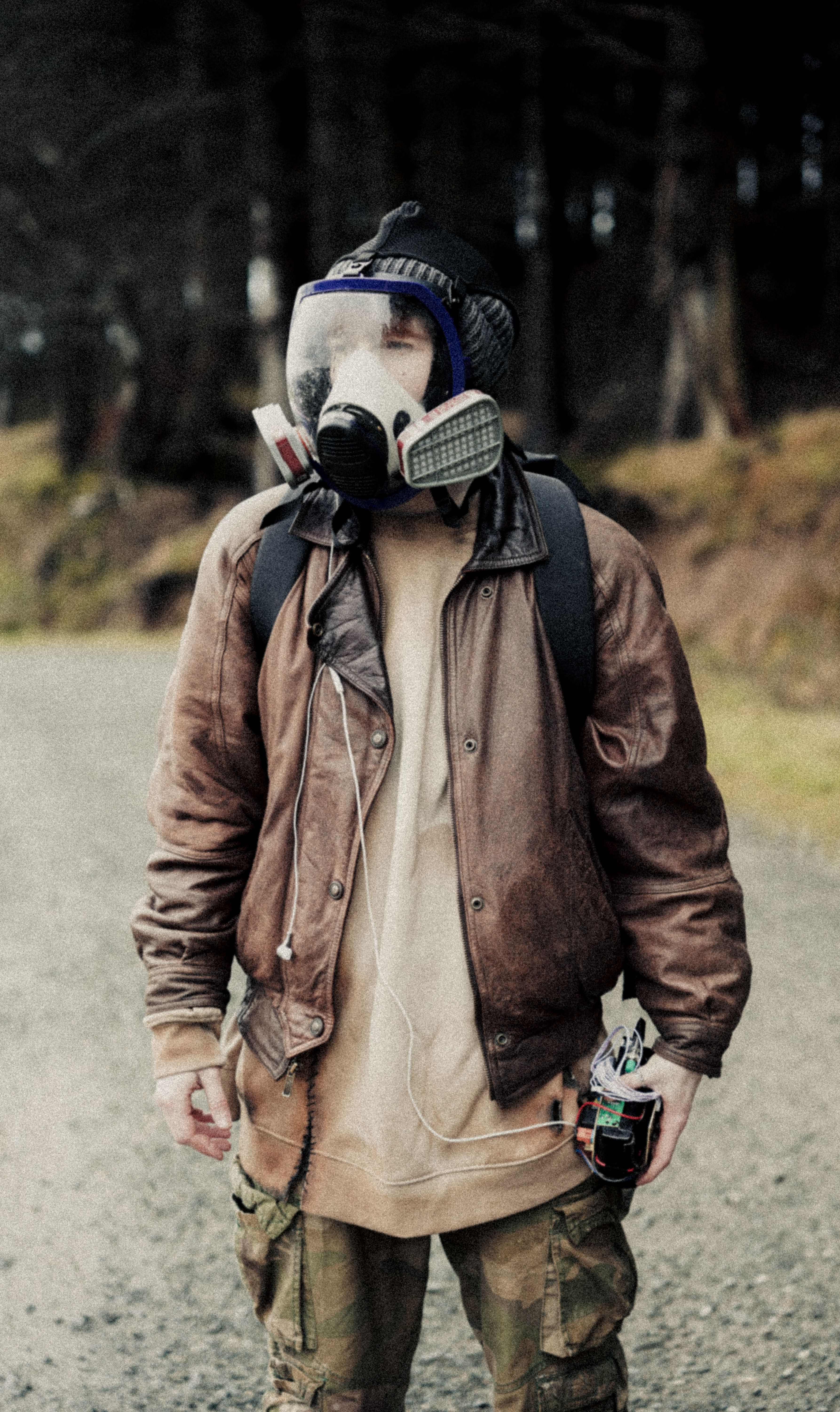 A person wearing a gas mask and holding a strange device in a forest landscape