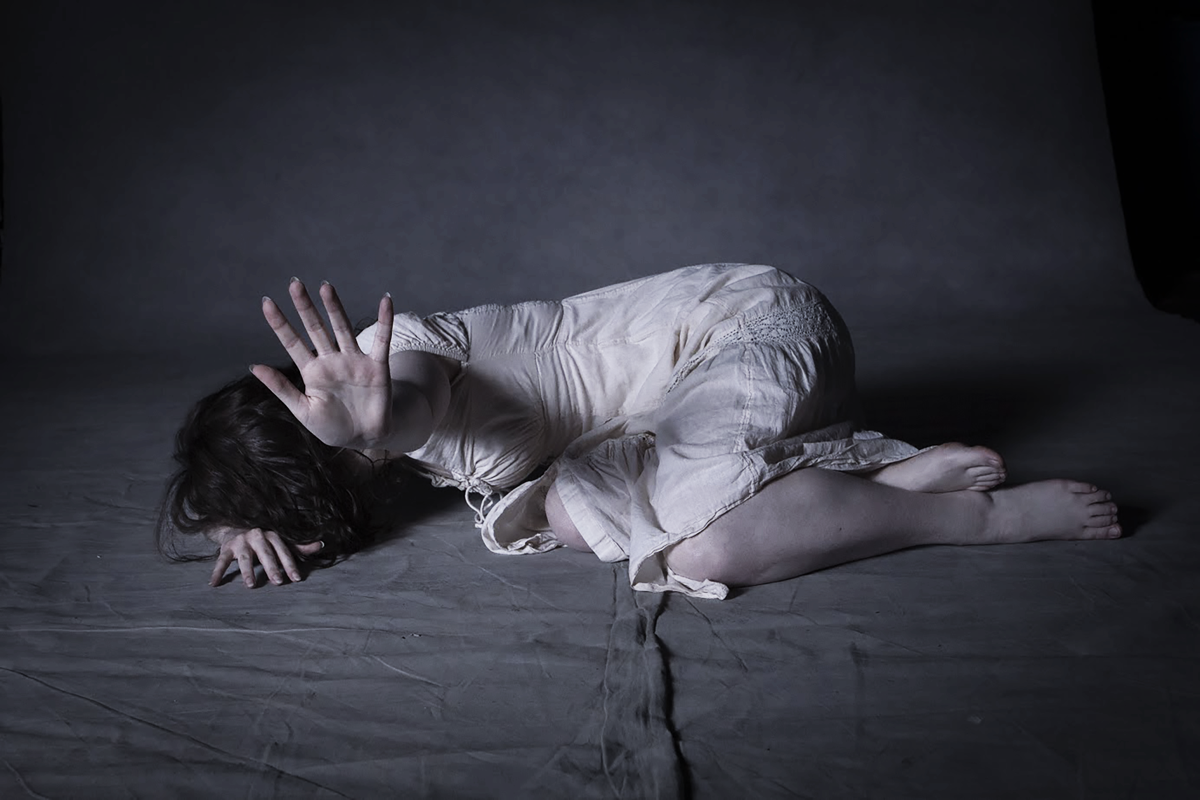 A scared fragile girl lying down on the floor trying to protect herself.