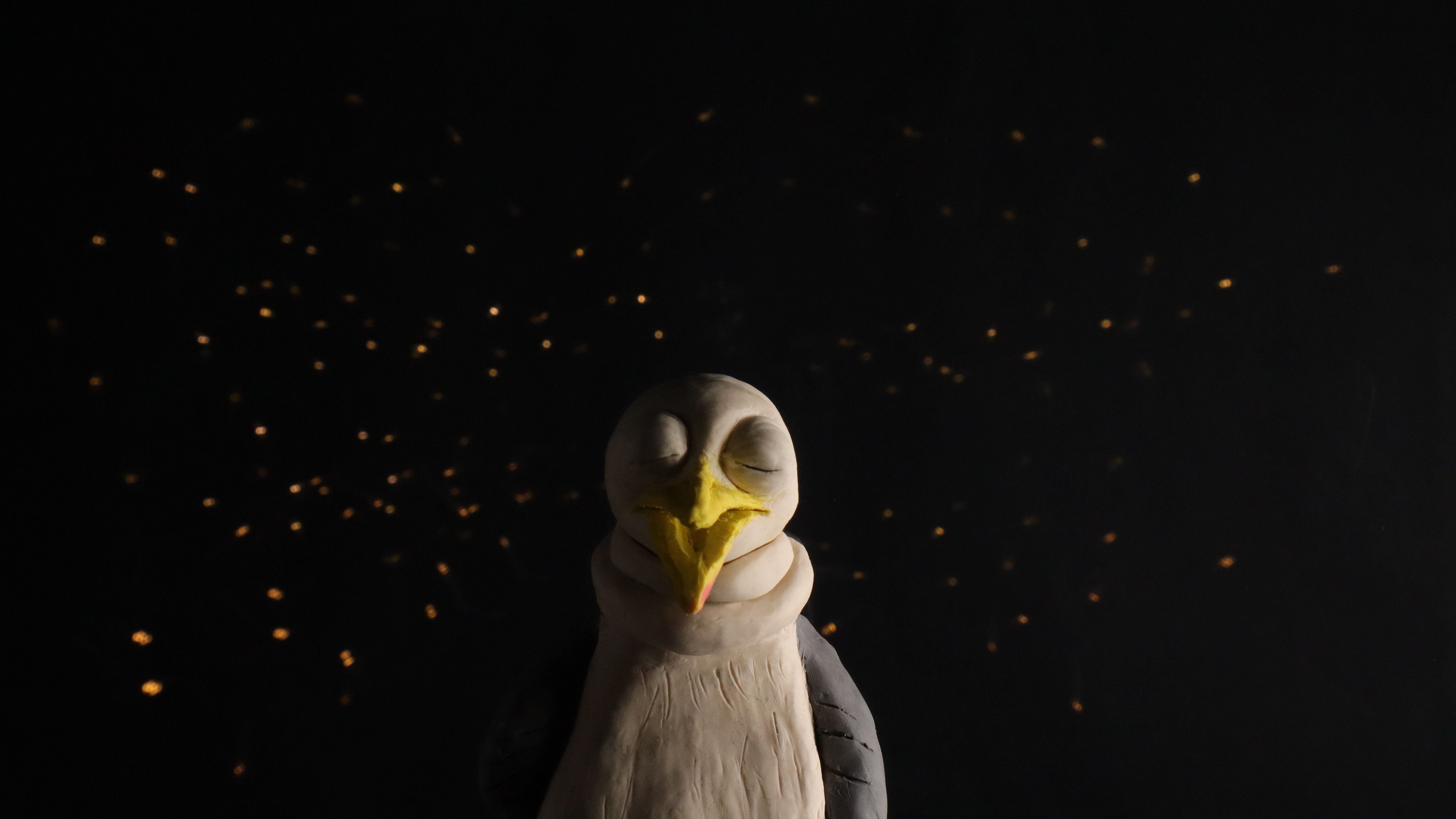 A still from Gullermo showing a plasticine gull with a squashed up neck on a dark background scattered with points of warm light like stars. 