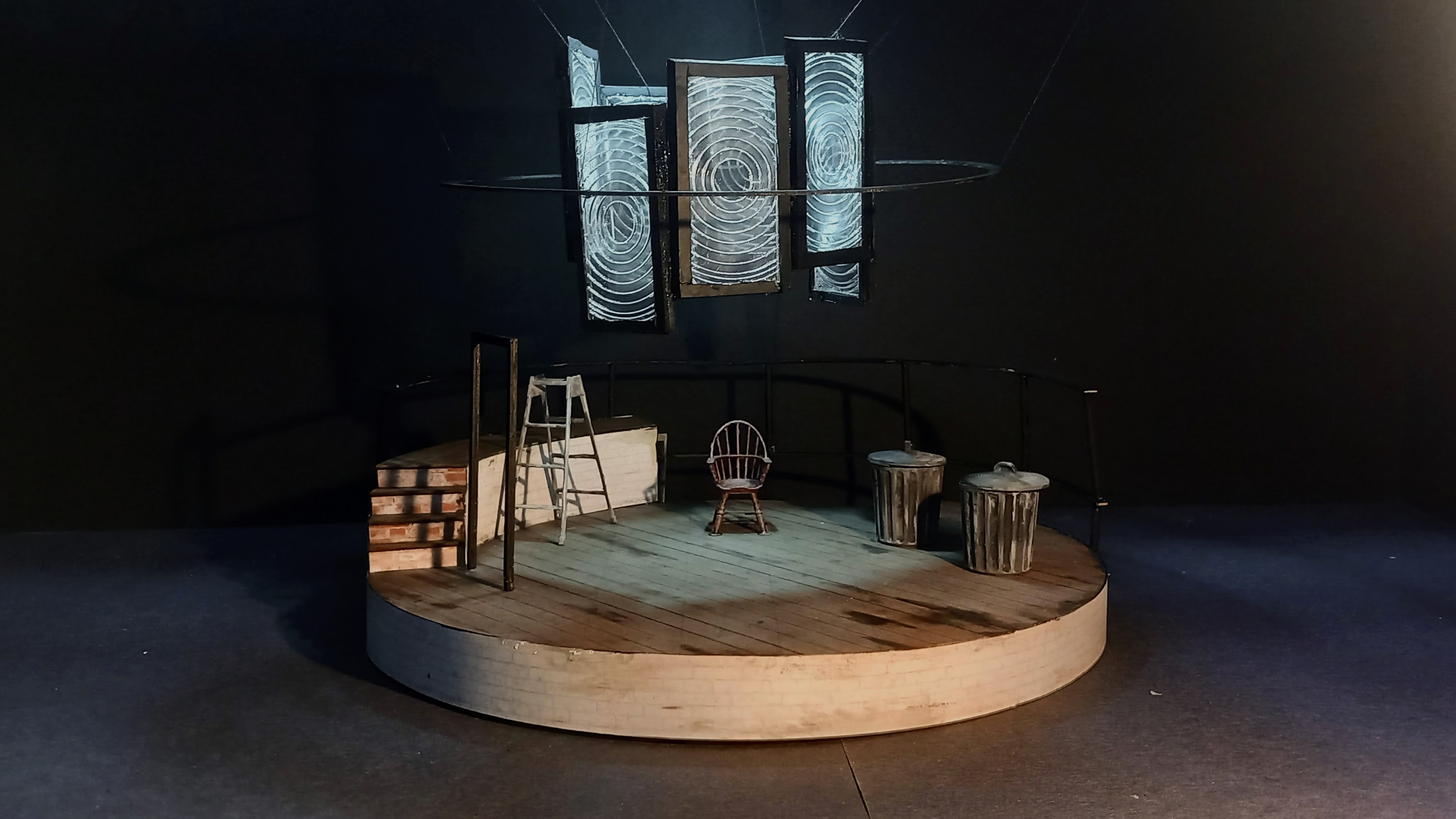 Miniature scale model of a circular stage, with large fresnel lens arranged in a circle hanging above the stage.