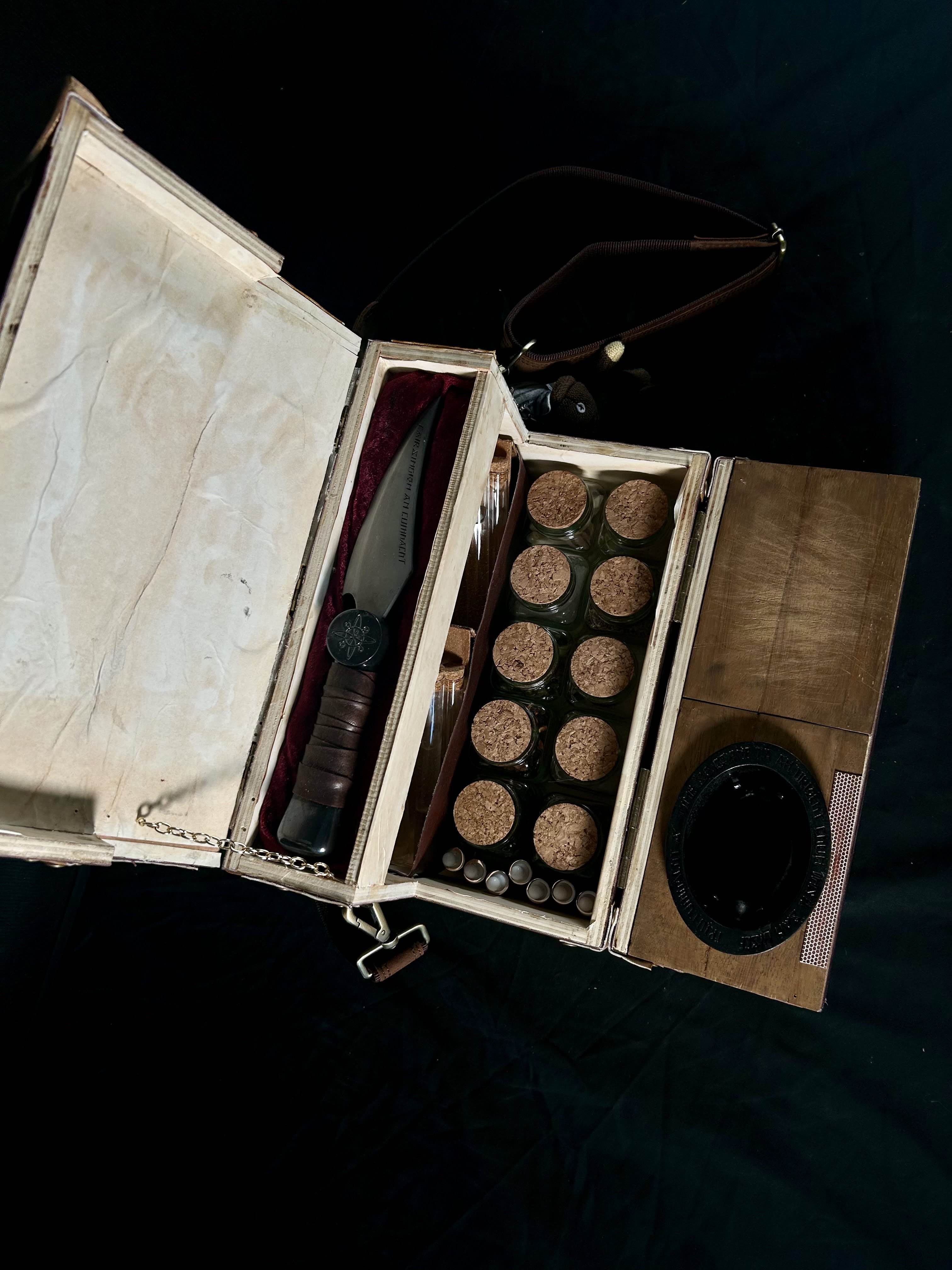Top-down image of the open box. The knife is on it's pillow, with ingredient jars beneath lined up in base of the box. The test tubes are directly below the knifes pillow.