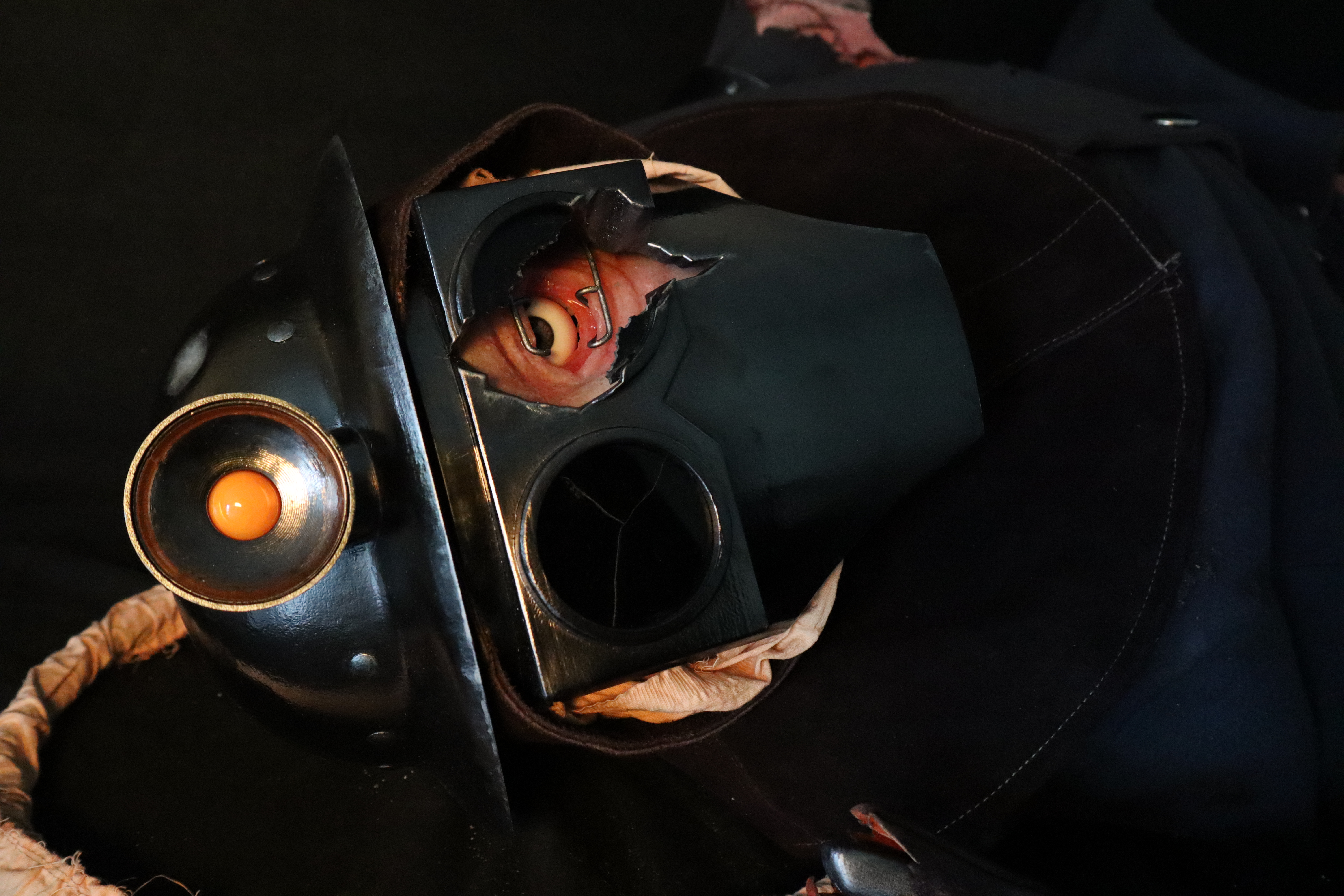 Close-up view of the soldier's head, showing the damaged faceplate, helmet and exposed eye & surrounding skin