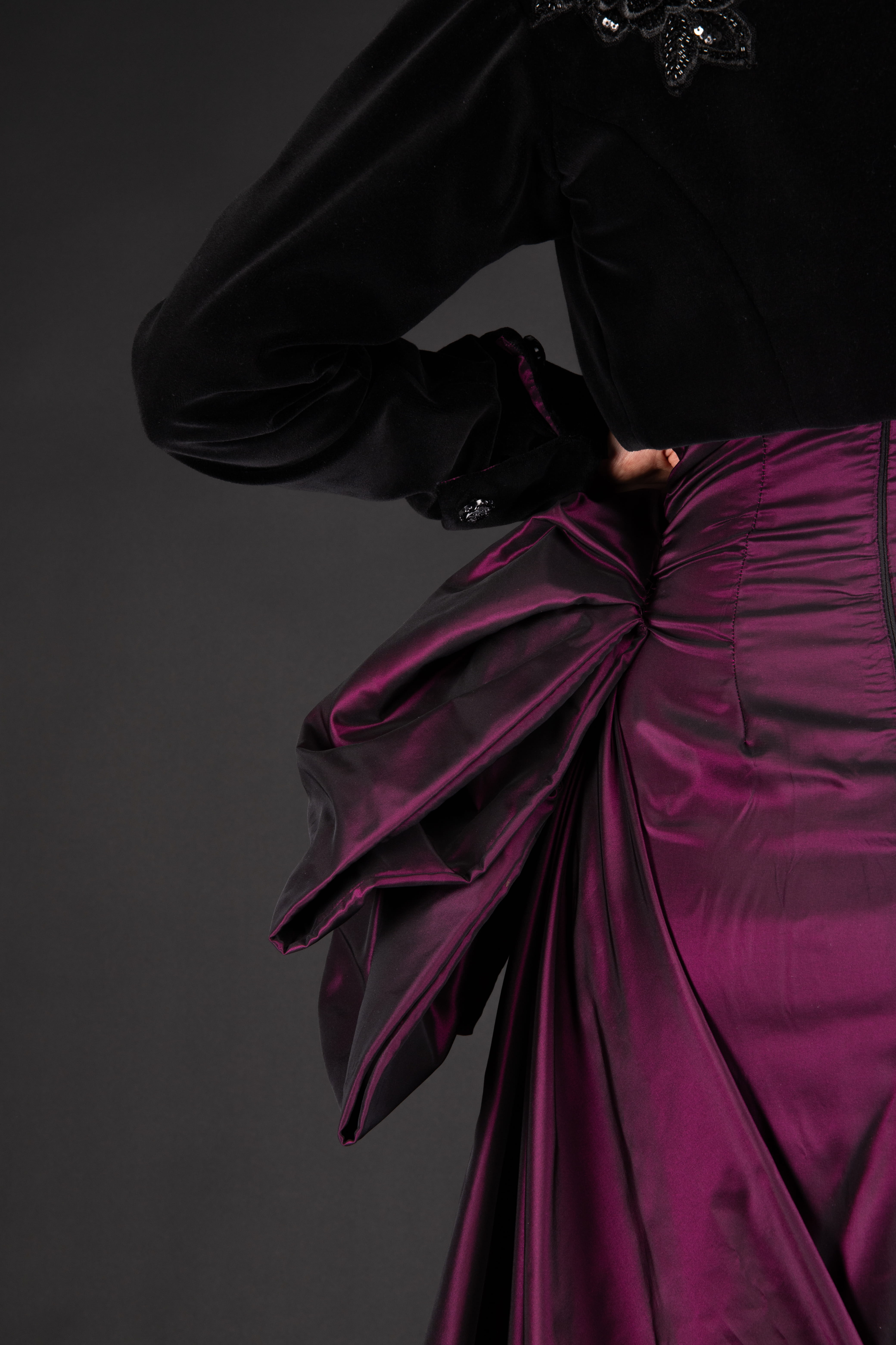 view of the back of the train and ribbon with hand on her waist and a light view of the beading on back of black velvet jacket