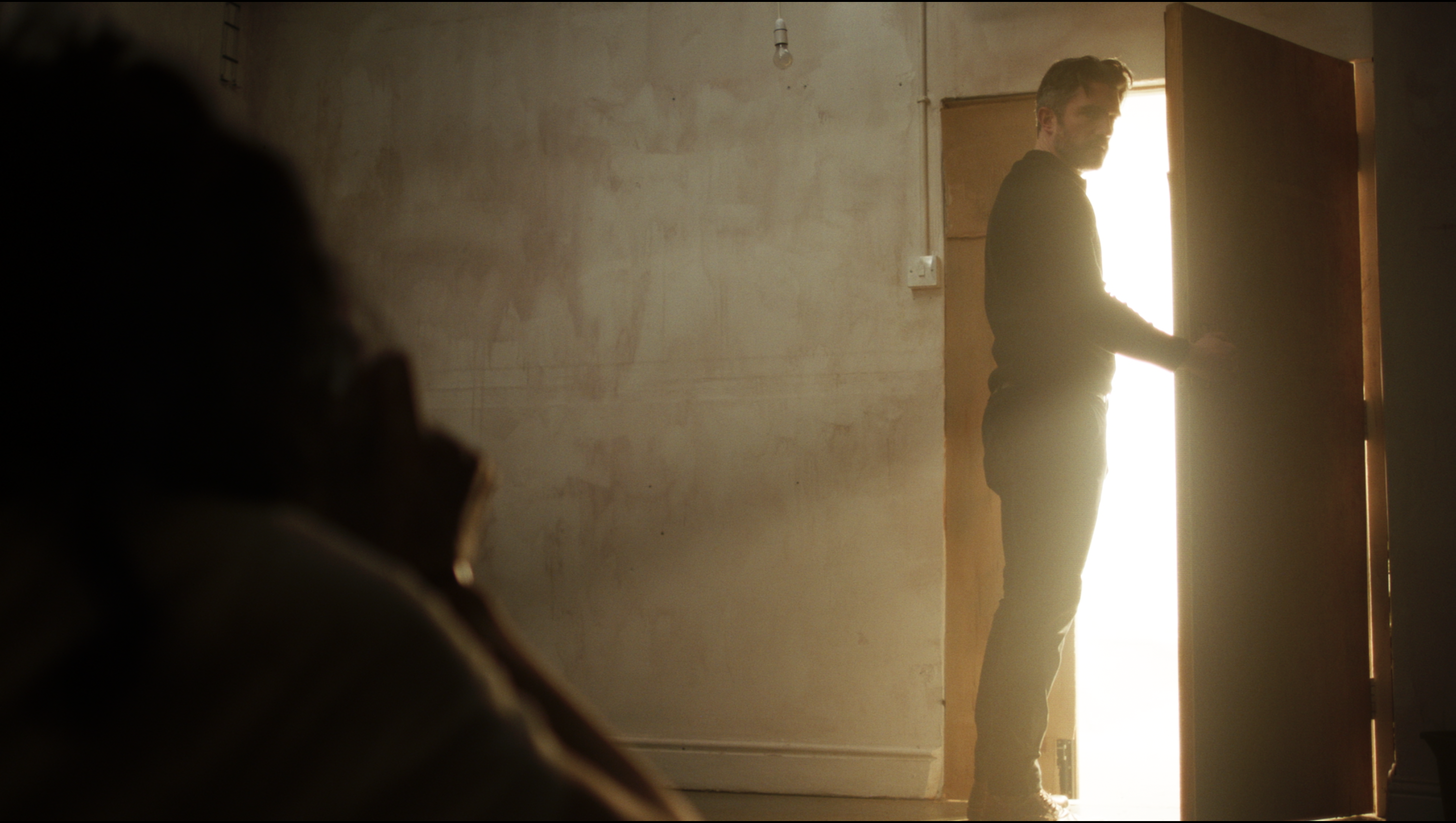 A man stands in front of a brightly lit open door