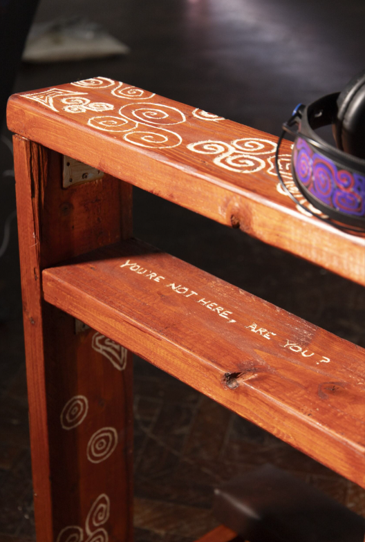 Personal prayer bench with celtic inspired carvings and headphones sitting on top, text reads "You're not here, Are You?"