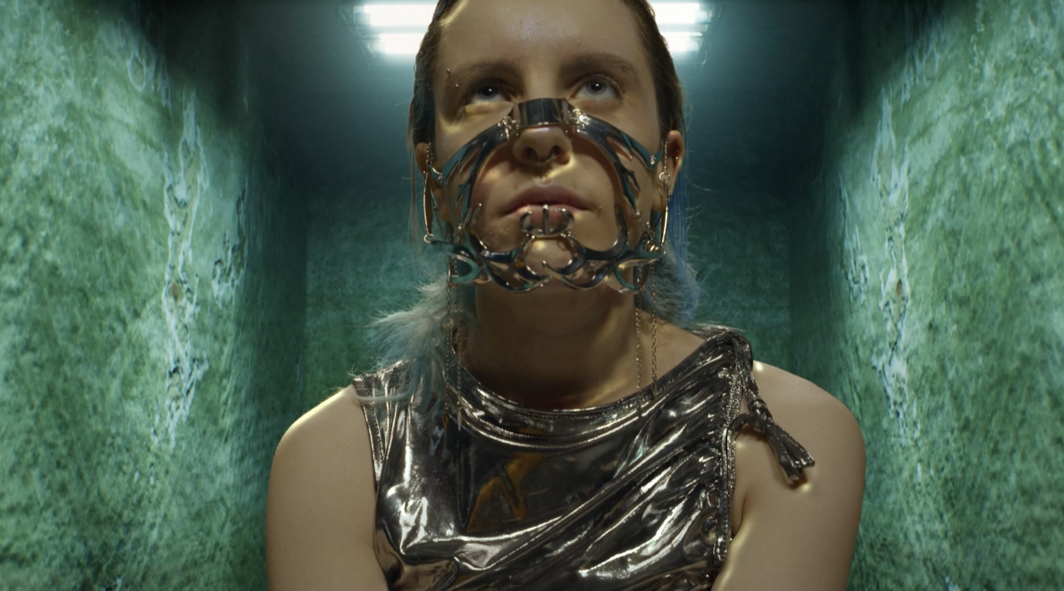 Woman with robotic features stares blankly at something behind camera
