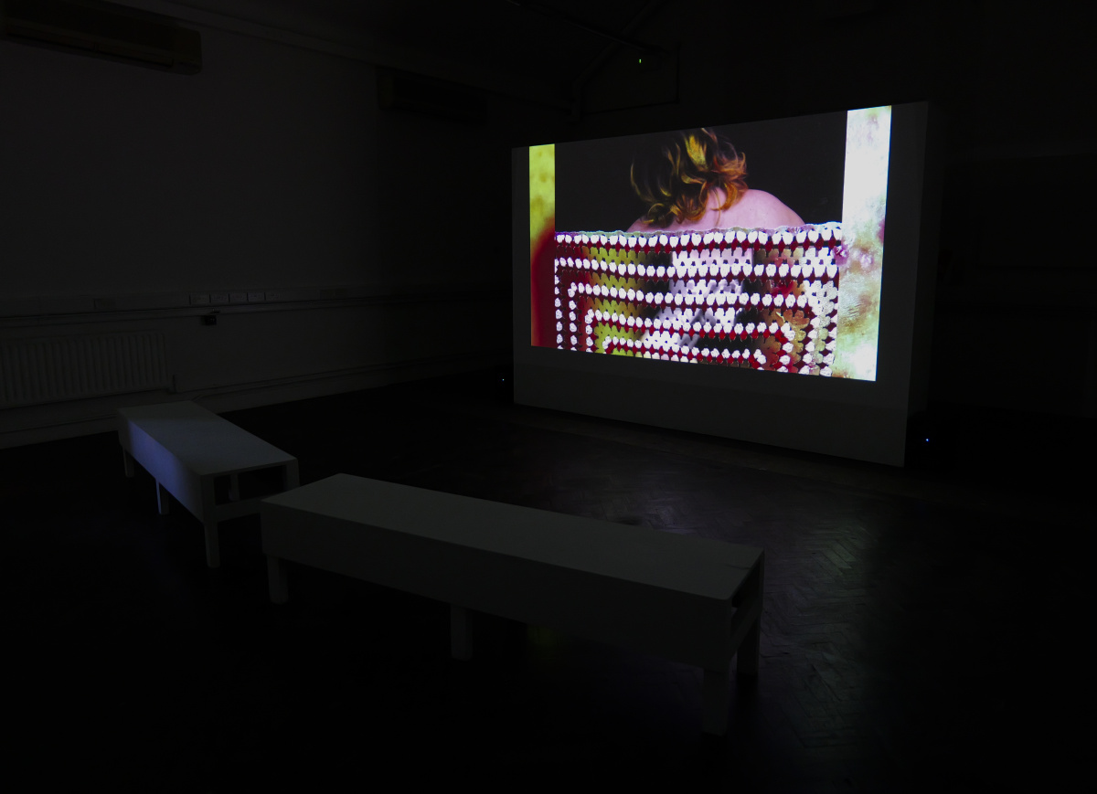 Diagonal Installation view of Cripteron piece, two benches are close to camera and a projection screen in the background, playing cripteron