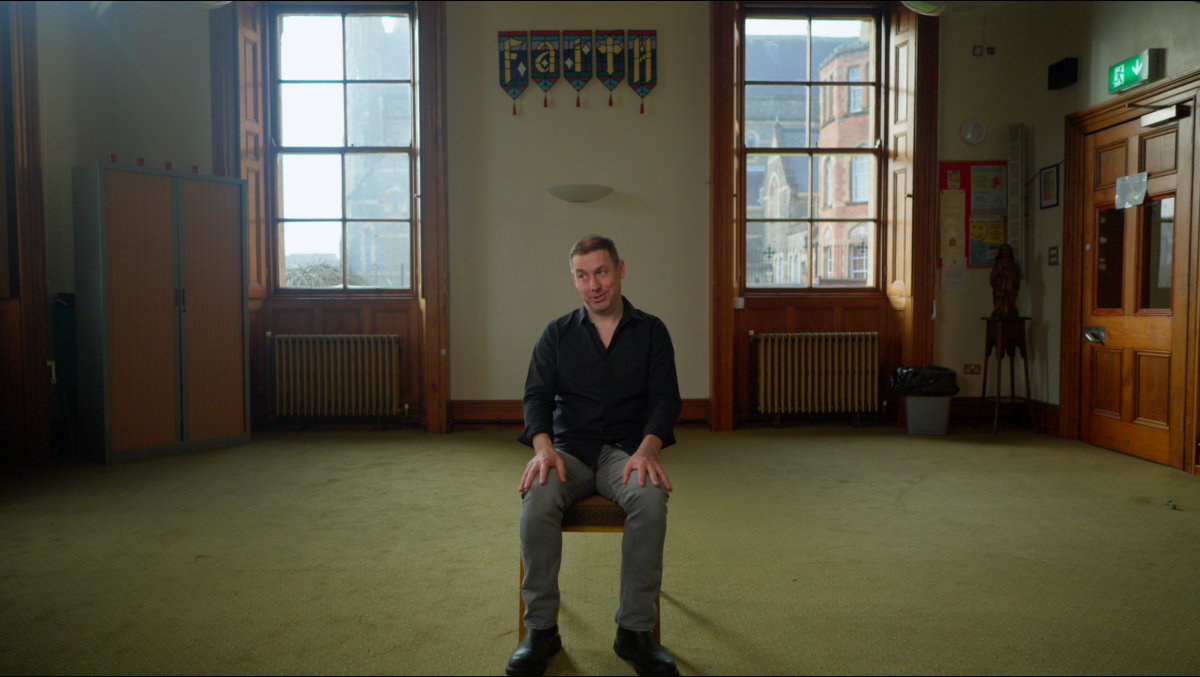 James in a big wide room with a wall hanging that spells faith above his head