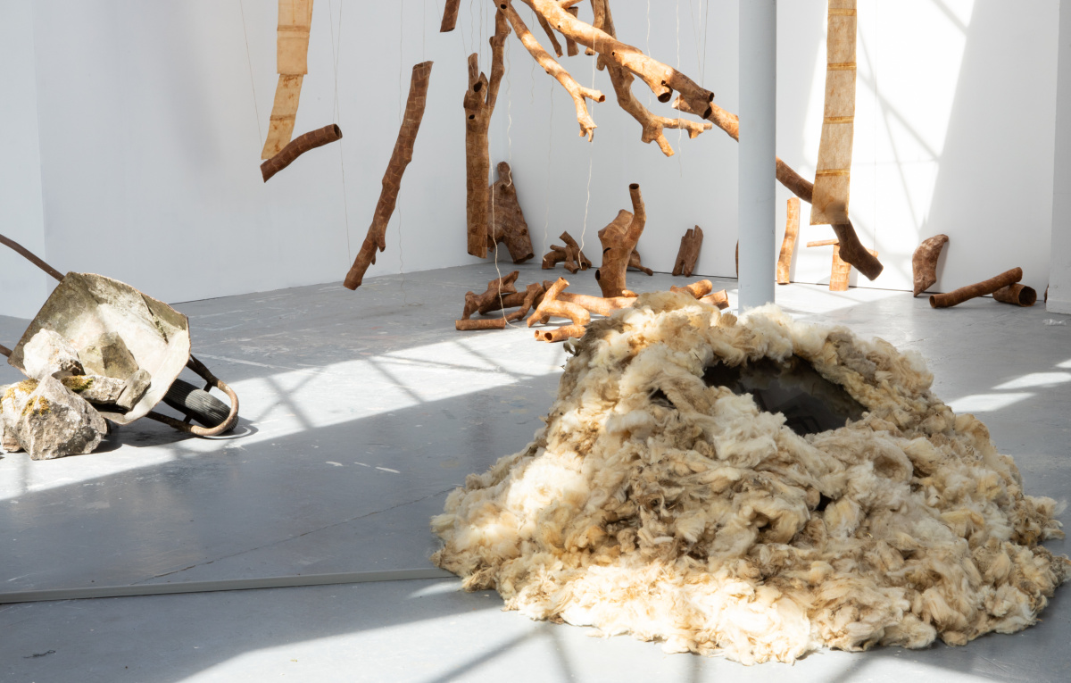 Wide shot, mound of raw sheep's wool with screen embedded, rusty wheelbarrow turned on side with big stones splaying out from it