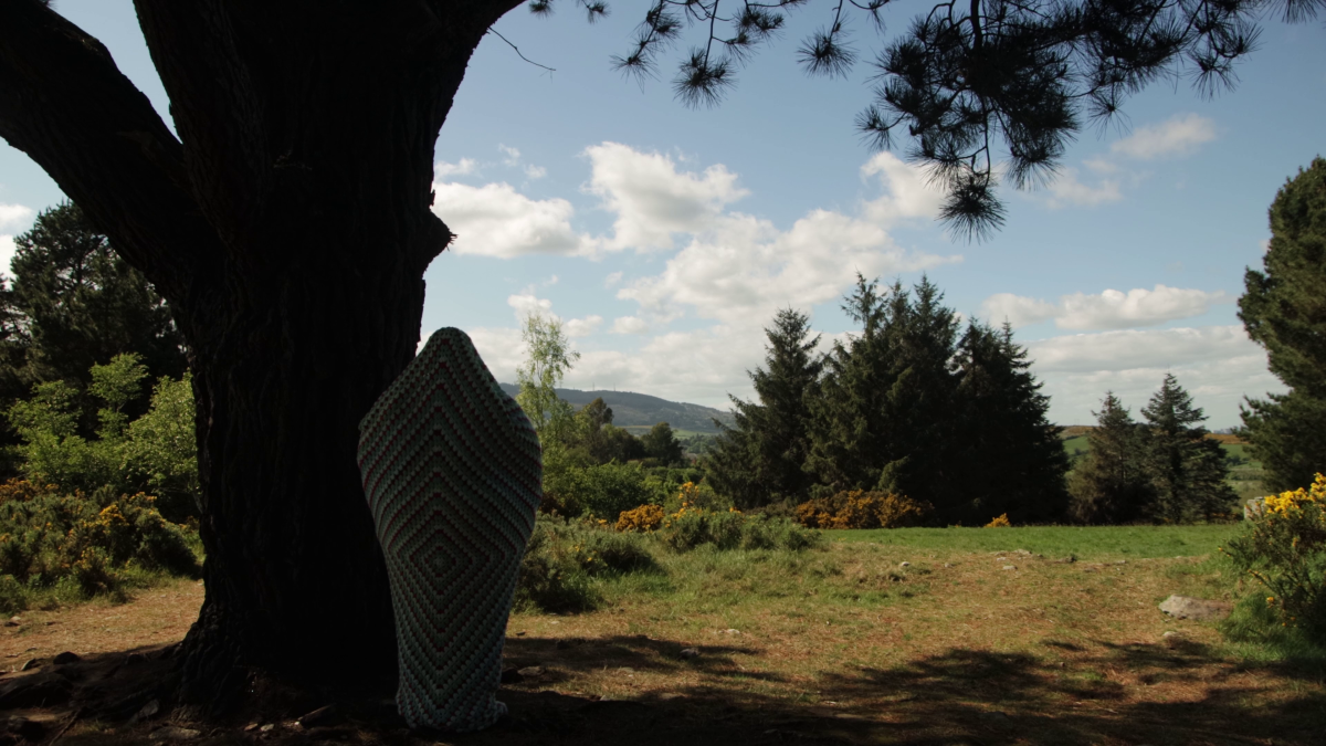 Logan Valentine in a Crocheted Cocoon, in the shade, looking out at a sunny field.