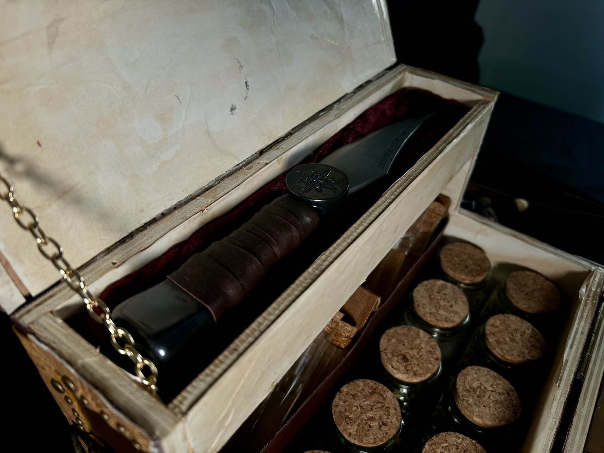 Close up of the knife inside the box, resting in it's velvet pillow. Underneath it are the ingredient jars and test tubes.
