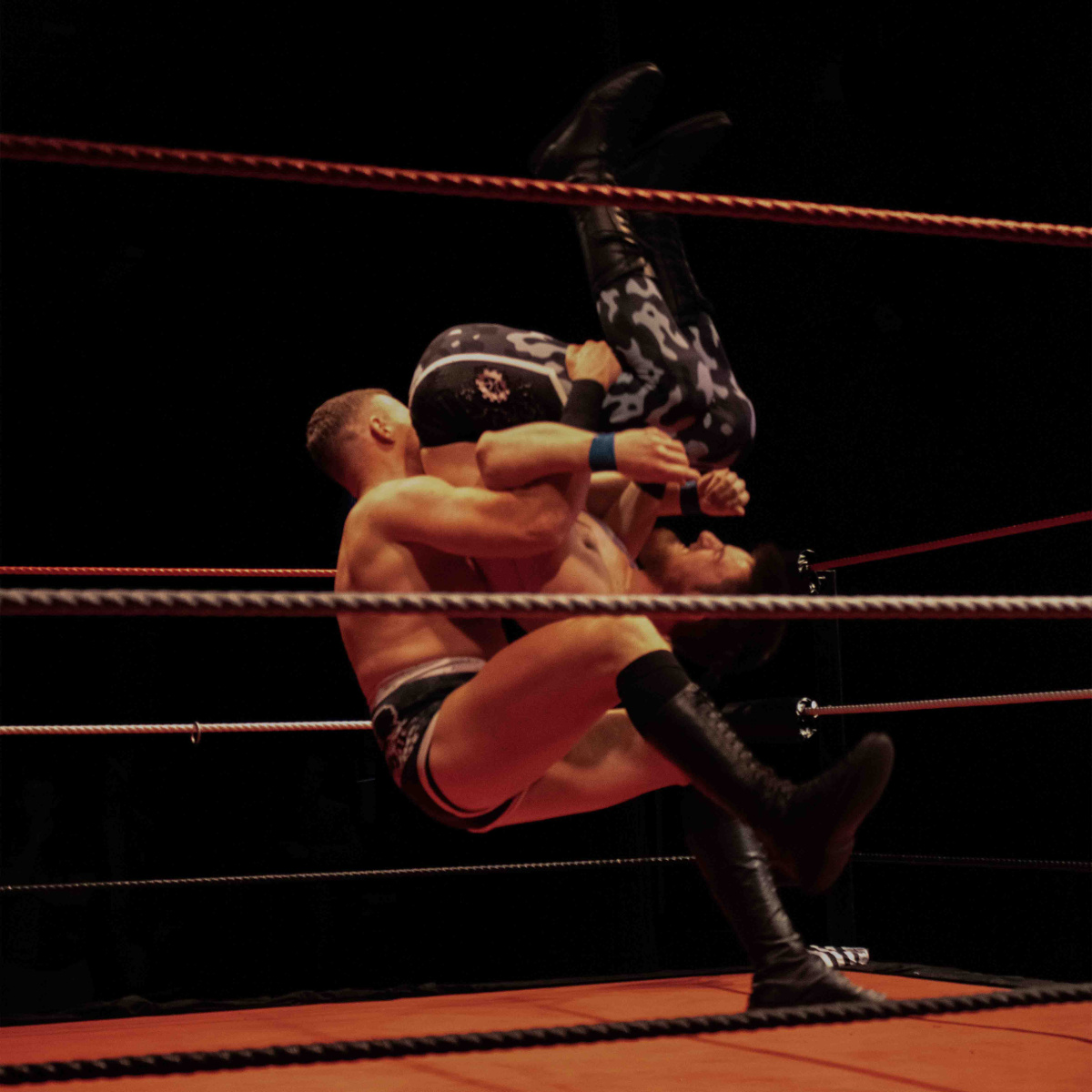 One man holding another man in the air, upside down. Both men are about to land on the floor of the ring