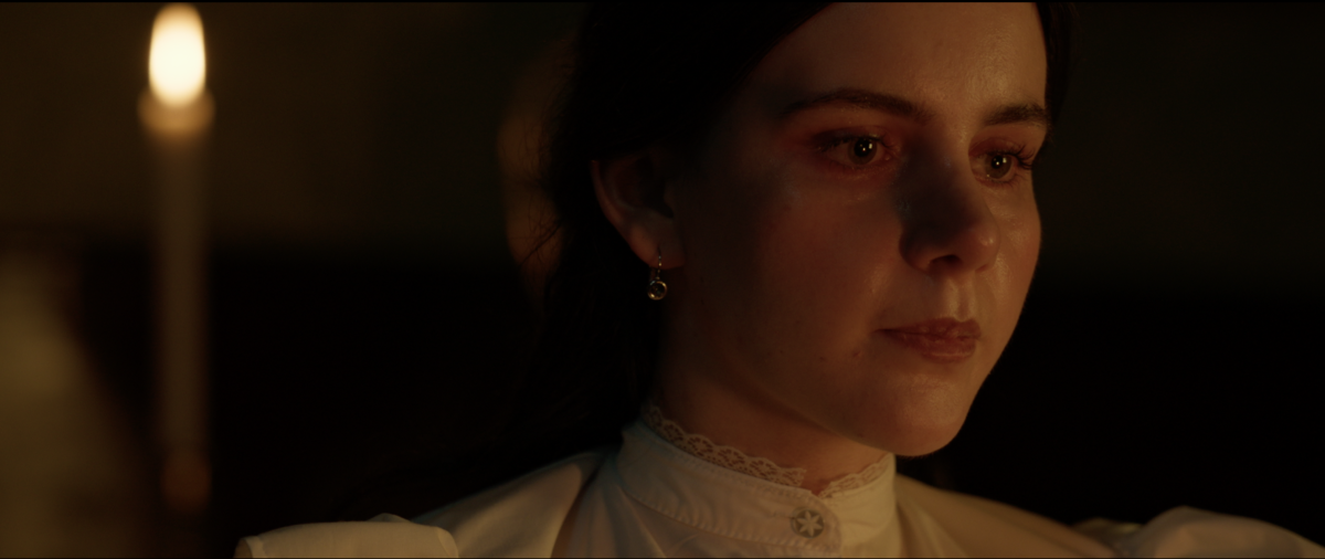 Nora (Claudia de Luca) sits at dinner with a candle in the background