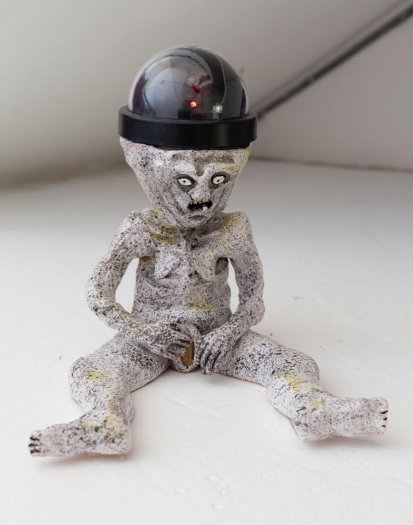 Image of a Sheela-na-gig with a CCTV camera on her head like a bowler hat