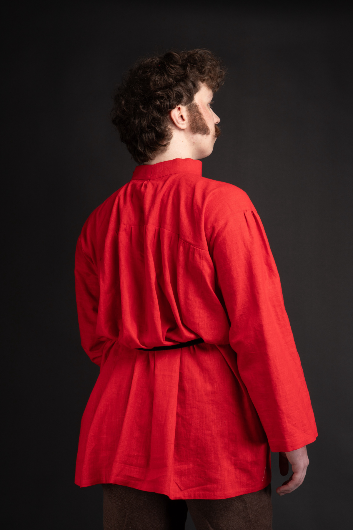 A man with sideburns and moustache in a red kosovorotka peasant shirt standing facing away from the viewer