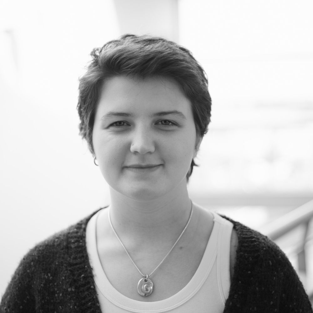 Ella is a woman with short dark hair. In the picture she is wearing a dark cardigan and a white tank top.