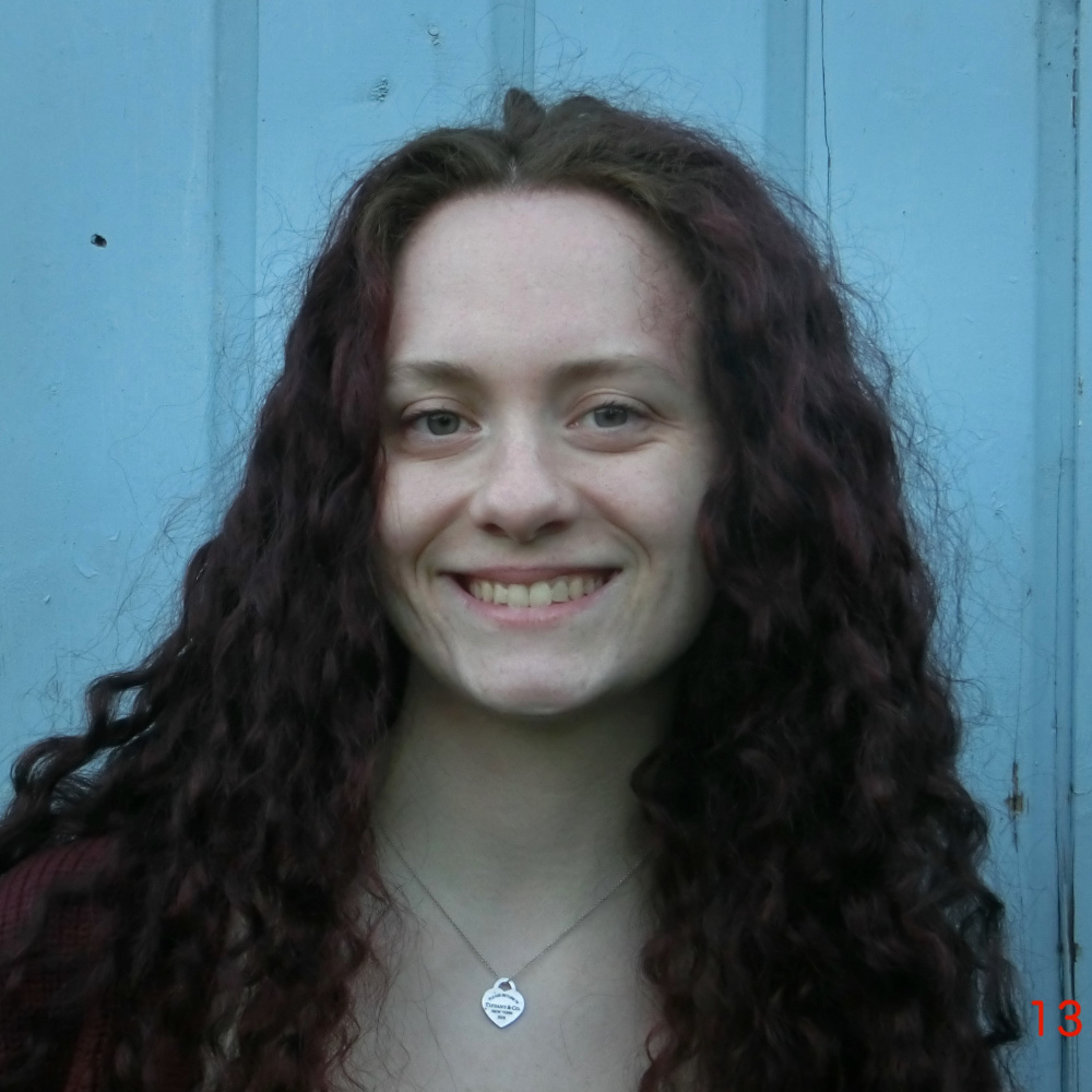 Photo of a smiling woman with curly hair from the shoulders upwards. 